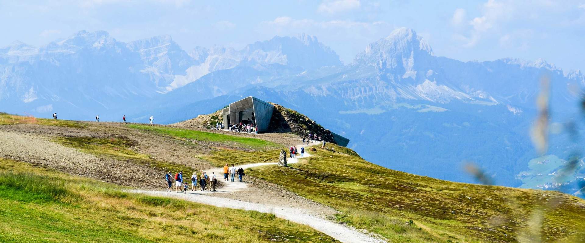 MMM Corones MMM Corones with visitors on top of Mt. Kronplatz & green meadows